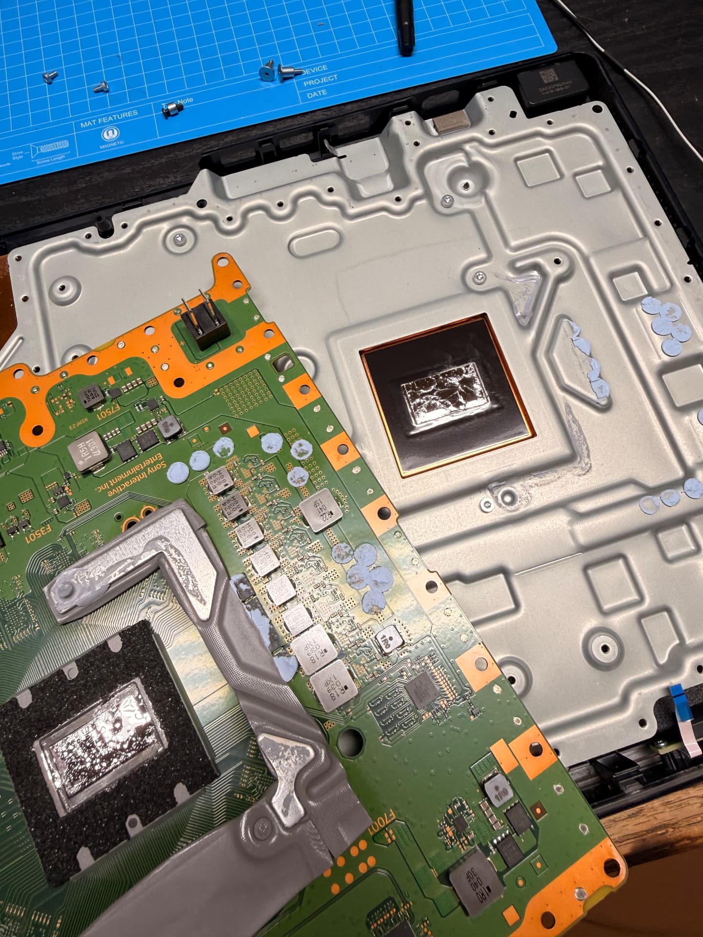 Disassembled PS5 motherboard and shield on the C’s Tech Shed workbench during liquid metal service